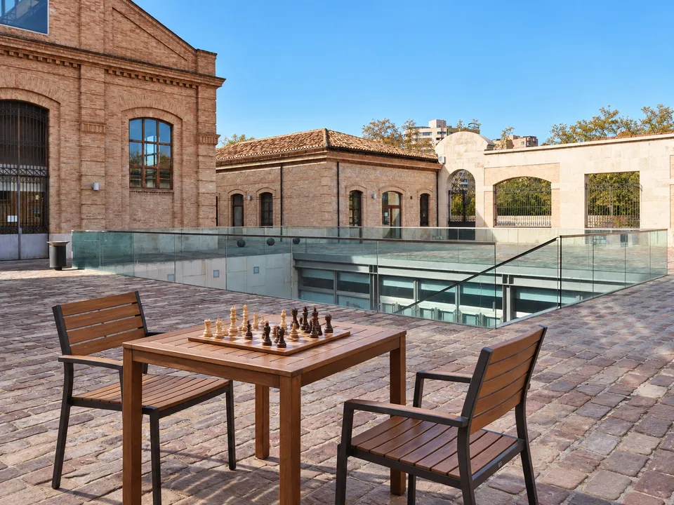 AI-generated illustration: empty Petxina courtyard with a wooden chess table, chessboard and two chairs.
